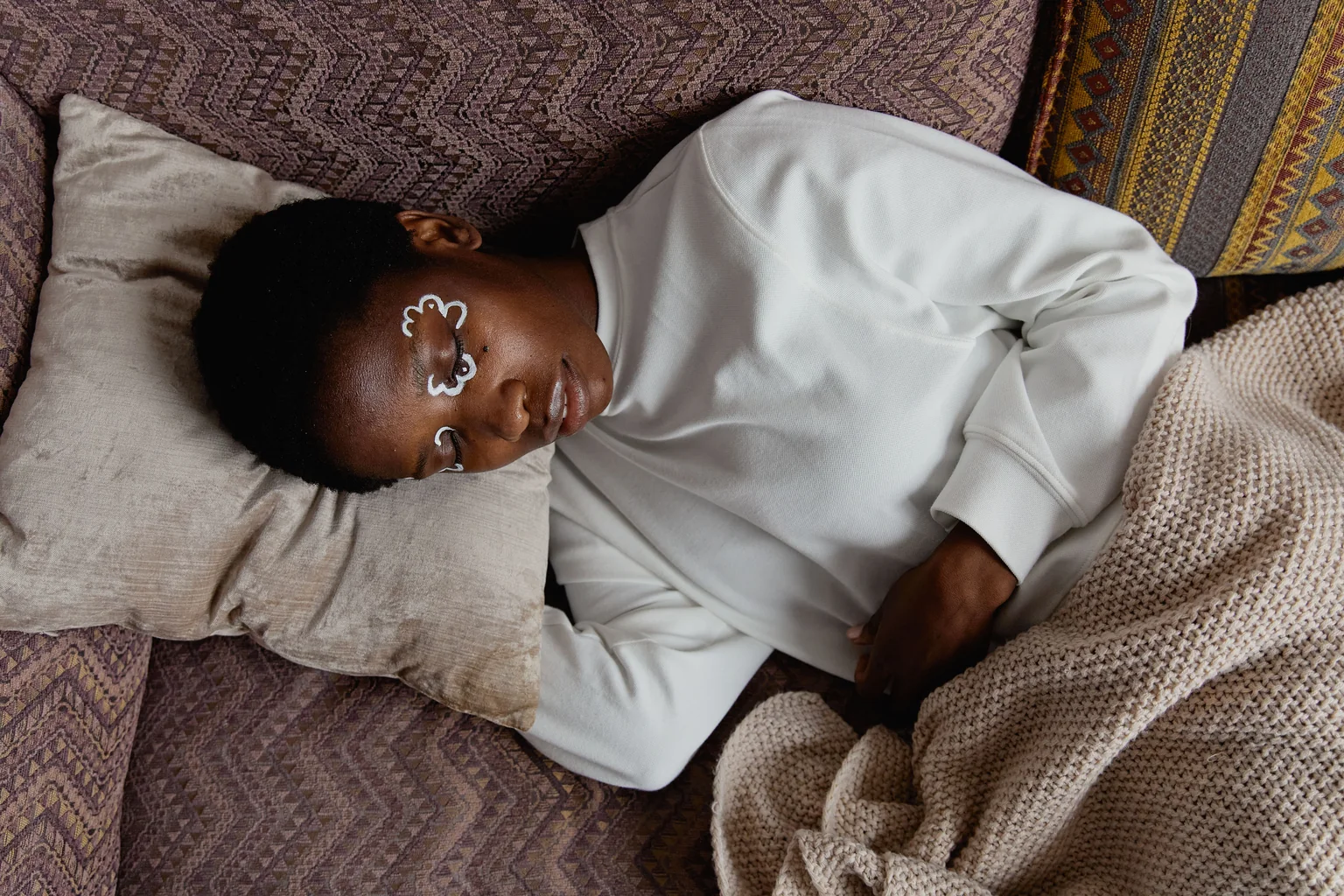 A person resting on a couch with eyes closed, wrapped in a blanket