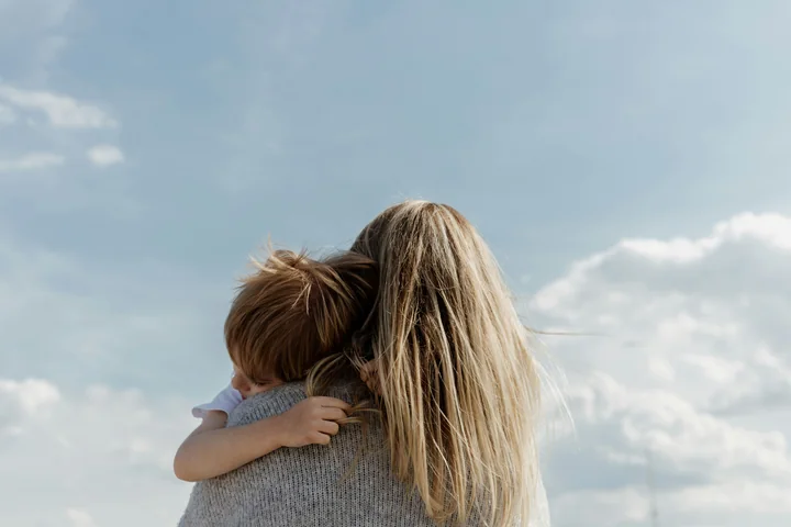 A mother holding her young child against an open sky