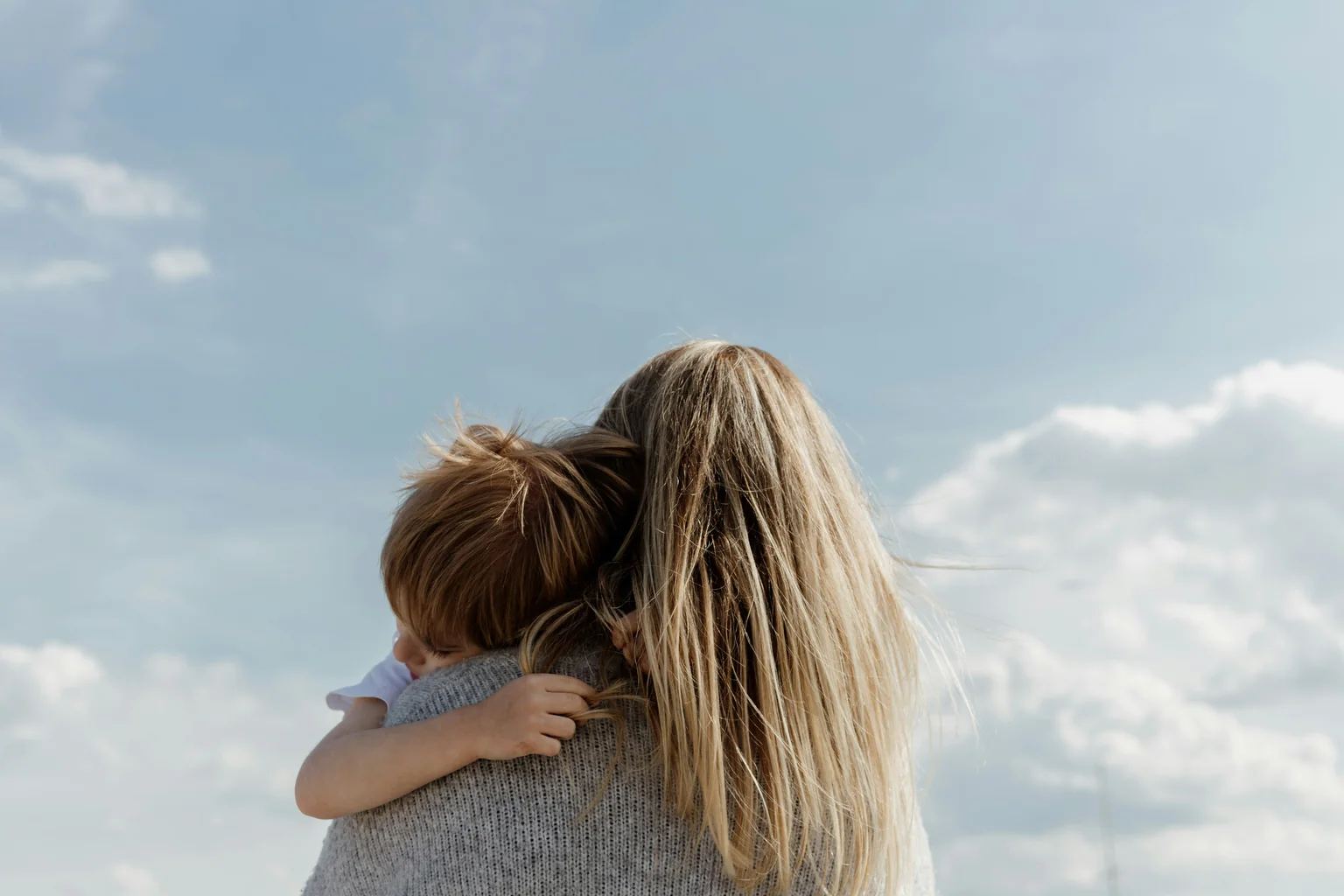 A mother holding her young child against an open sky