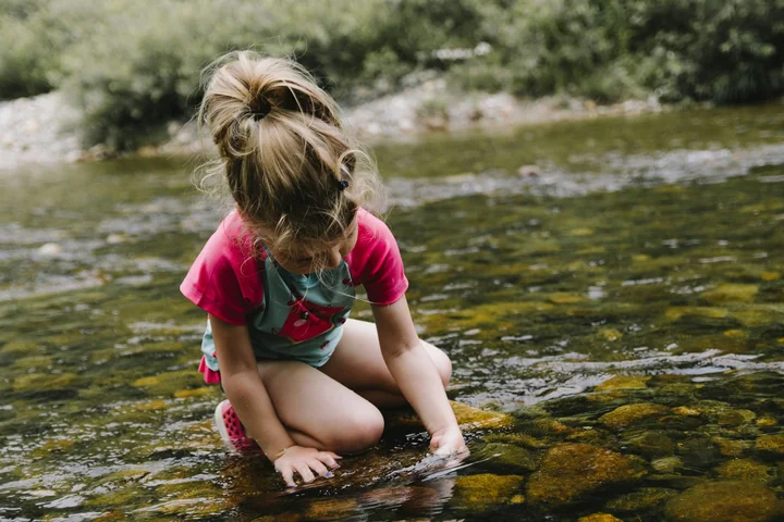 A young child crouched and absorbed in playing at the edge of a stream