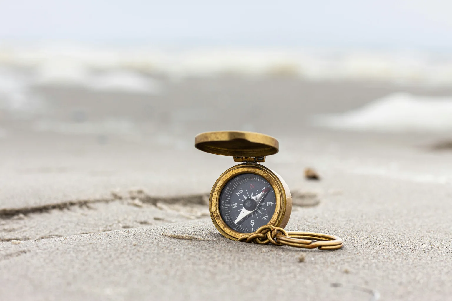 A brass compass resting open on sand