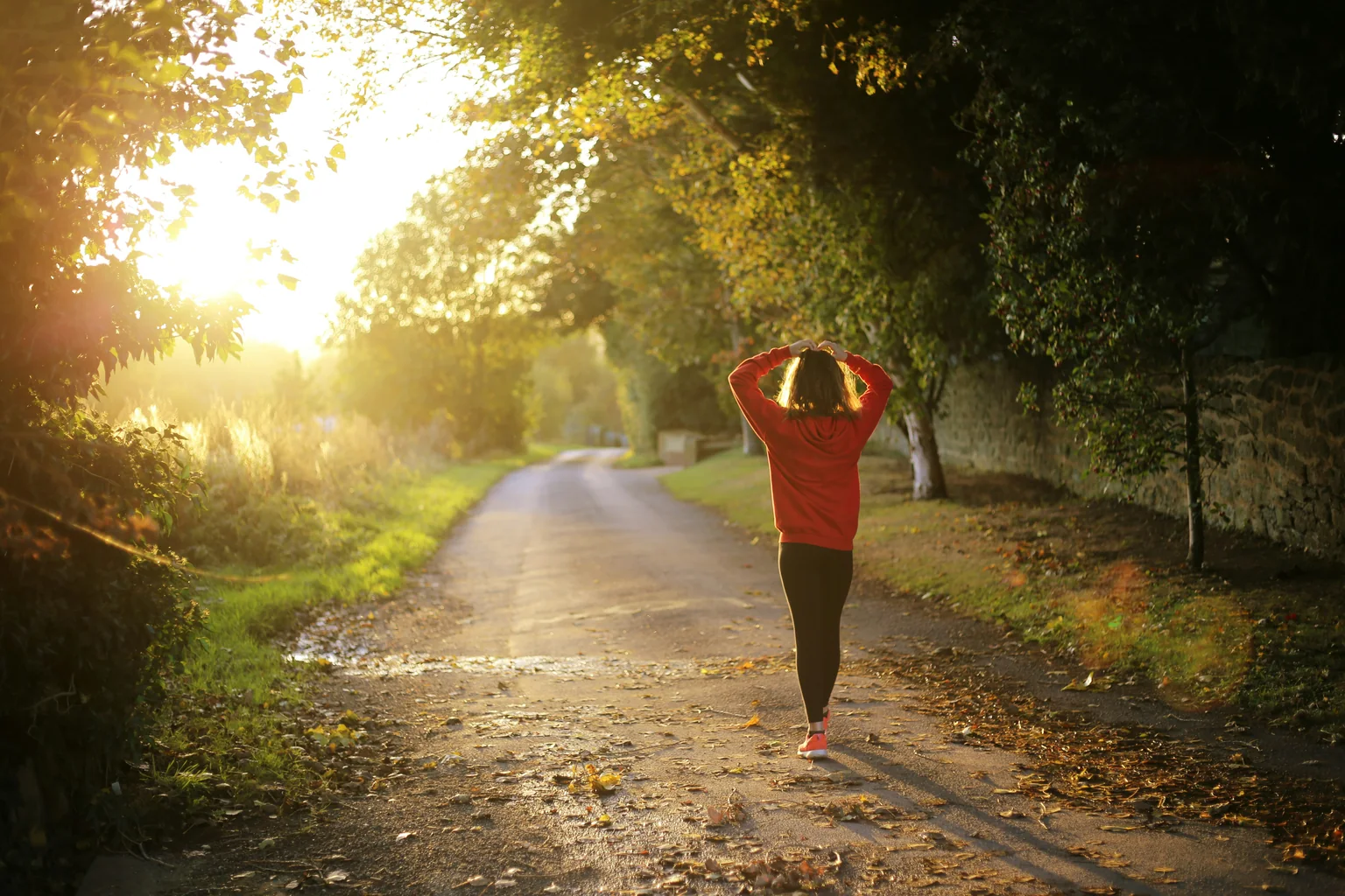 A woman walking forward down a quiet path into golden morning light