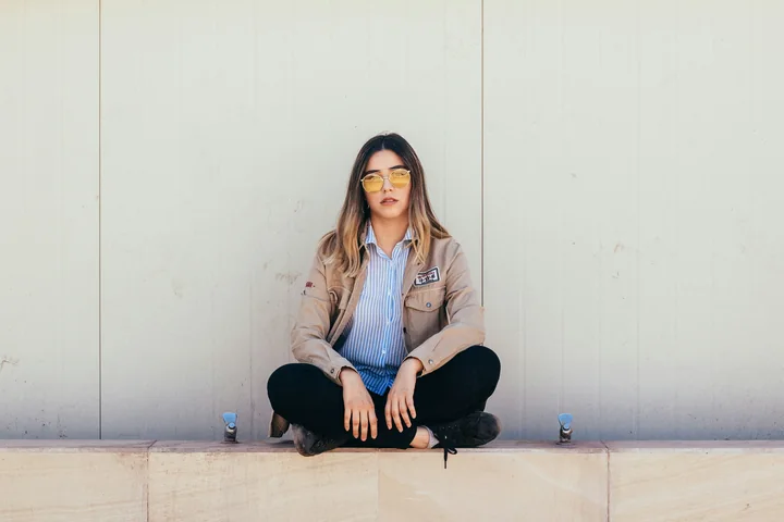 A woman sitting calmly cross-legged against a pale wall