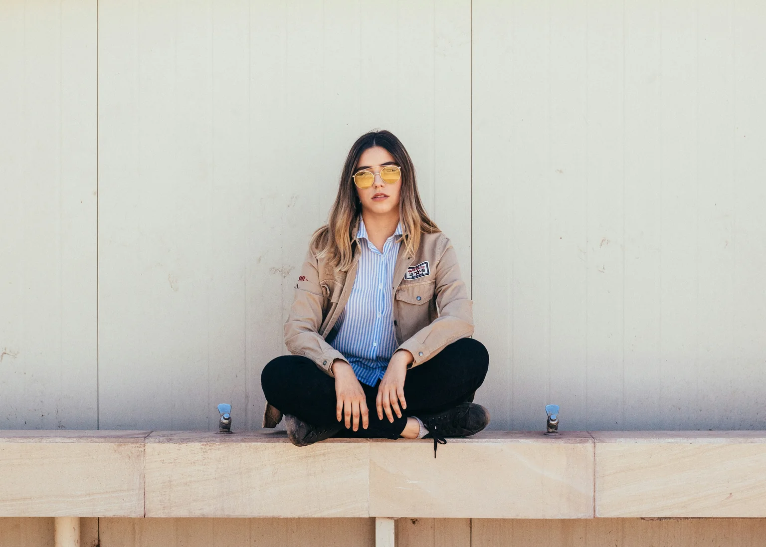 A woman sitting calmly cross-legged against a pale wall
