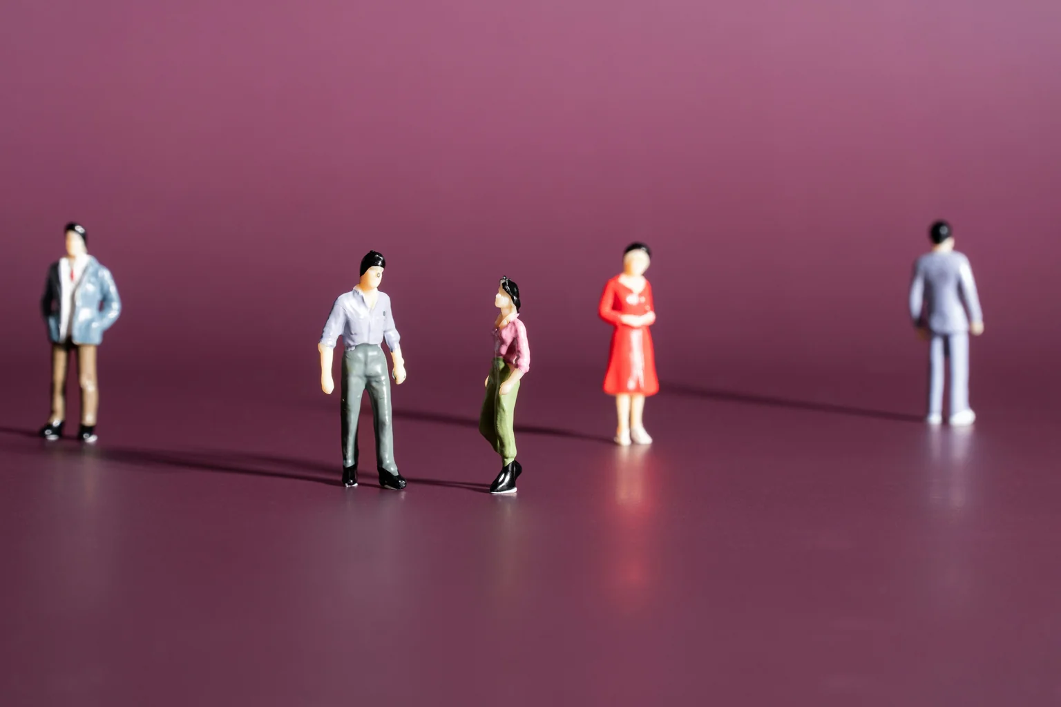 Small figures standing apart on a deep plum background, one set off alone